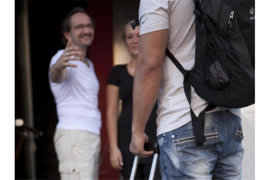 Ein Erwachsener (r) steht mit einem Rollkoffer in der Hand vor einem älteren Paar. Foto: Silvia Marks/Archivbild