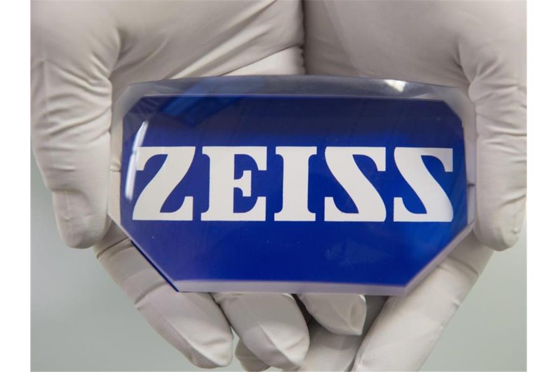 Ein Facharbeiter hält eine Linse mit dem Schriftzug „Zeiss“ in seinen Händen. Foto: Sebastian Kahnert/zb/dpa/Archivbild