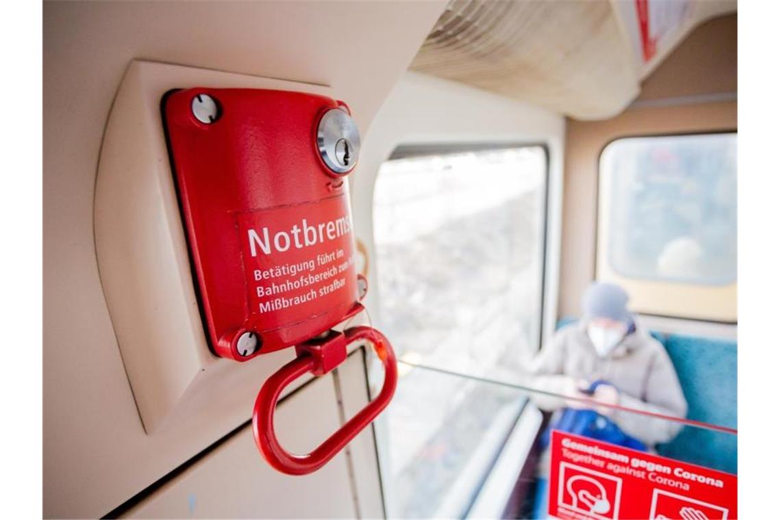 Ein Fahrgast mit Mund-Nasen-Schutz sitzt in einer Berliner S-Bahn hinter der Notbremse. Foto: Christoph Soeder/dpa