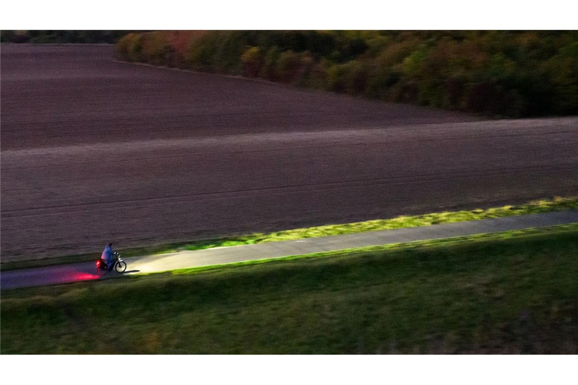 Ein Fahrradfahrer fährt am frühen Morgen mit Licht über einen Feldweg bei Hannover.