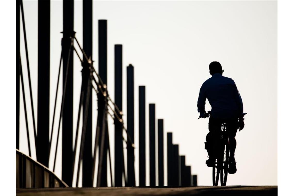 Ein Fahrradfahrer fährt am frühen Morgen über eine Brücke im niedersächsischen Laatzen. Foto: Julian Stratenschulte