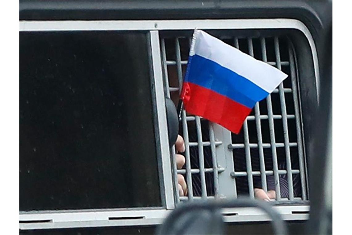 Hunderte bei Kundgebung in Moskau festgenommen Ein festgenommener Demonstrant schwenkt aus einem Polizeiwagen heraus eine kleine russische Fahne. Foto: Pavel Golovkin/AP