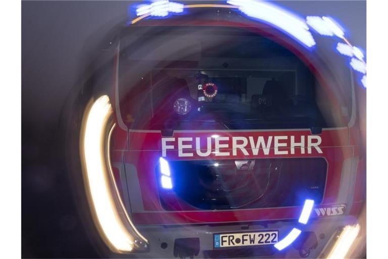 Ein Feuerwehrfahrzeug steht mit eingeschaltetem Blaulicht im Sonnenuntergang auf einer Straße. Foto: Patrick Seeger/dpa