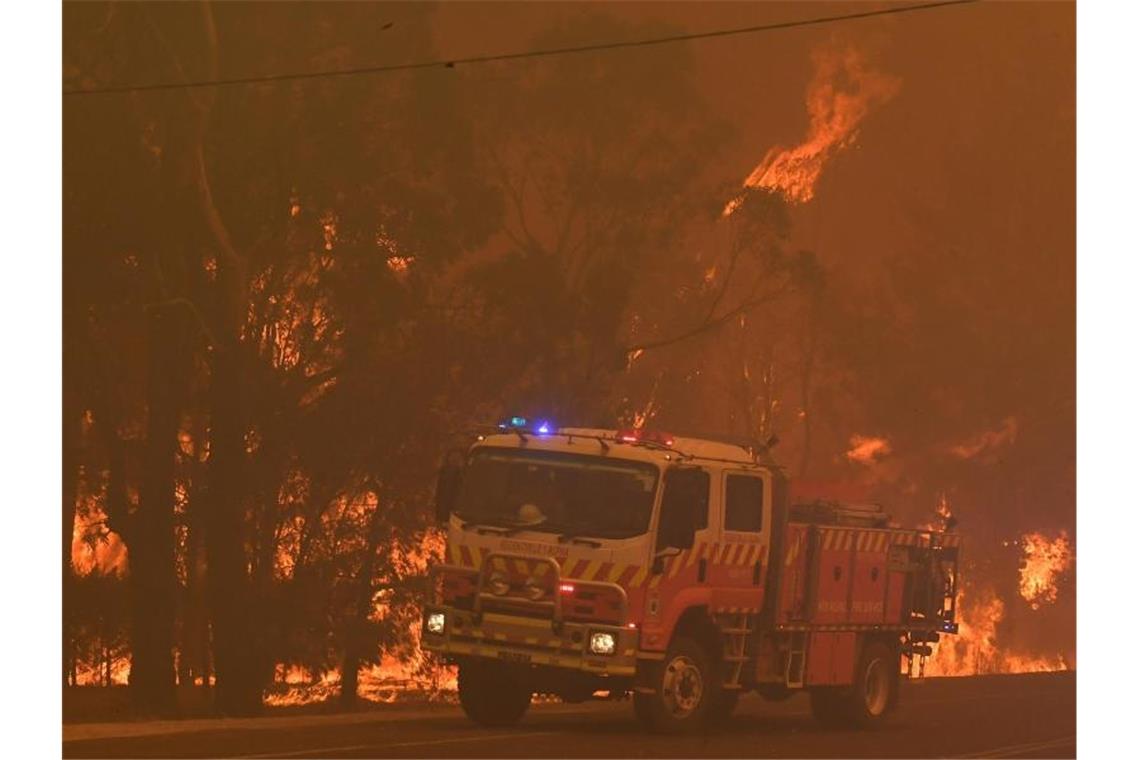 Ein Feuerwehrfahrzeug steht südwestlich von Sydney bei einem Buschbrand neben Bäumen, die Feuer gefangen haben. Foto: Dean Lewins/AAP/dpa
