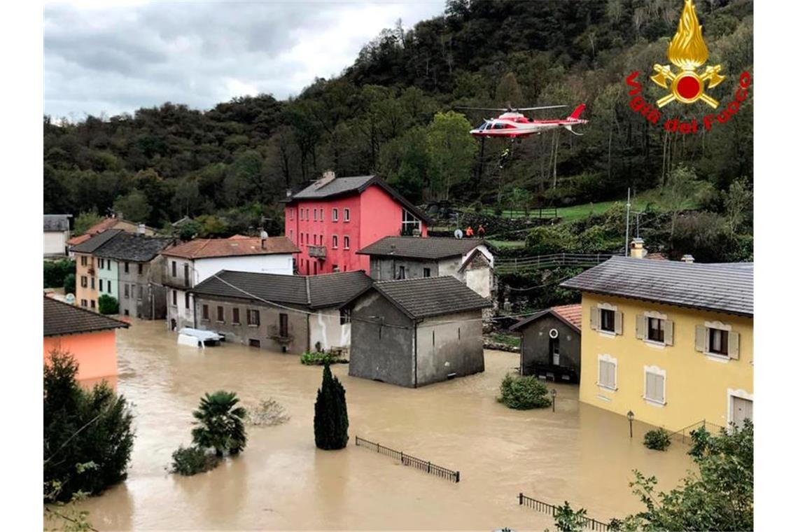 Ein Feuerwehrhubschrauber überfliegt die überschwemmte Stadt Ornavasso in der norditalienischen Region Piemont. Foto: -/Vigili del Fuoco/dpa