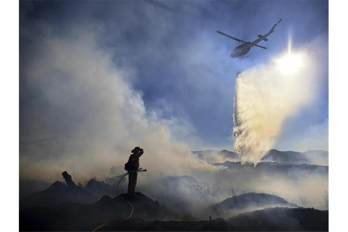 Weiter extreme Hitze im Westen der USA Ein Feuerwehrmann ist bei einem Waldbrand im Einsatz, während ein Löschhubschrauber Wasser abwirft. Foto: Kent Porter/The Press Democrat/AP/dpa