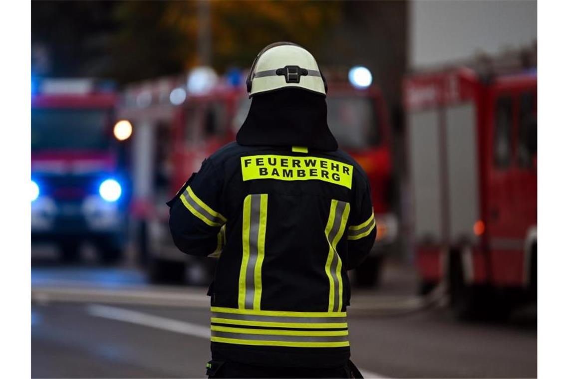 Ein Feuerwehrmann steht bei Nachlöscharbeiten vor mehreren Feuerwehreinsatzfahrzeugen. Foto: Nicolas Armer/dpa/Archivbild