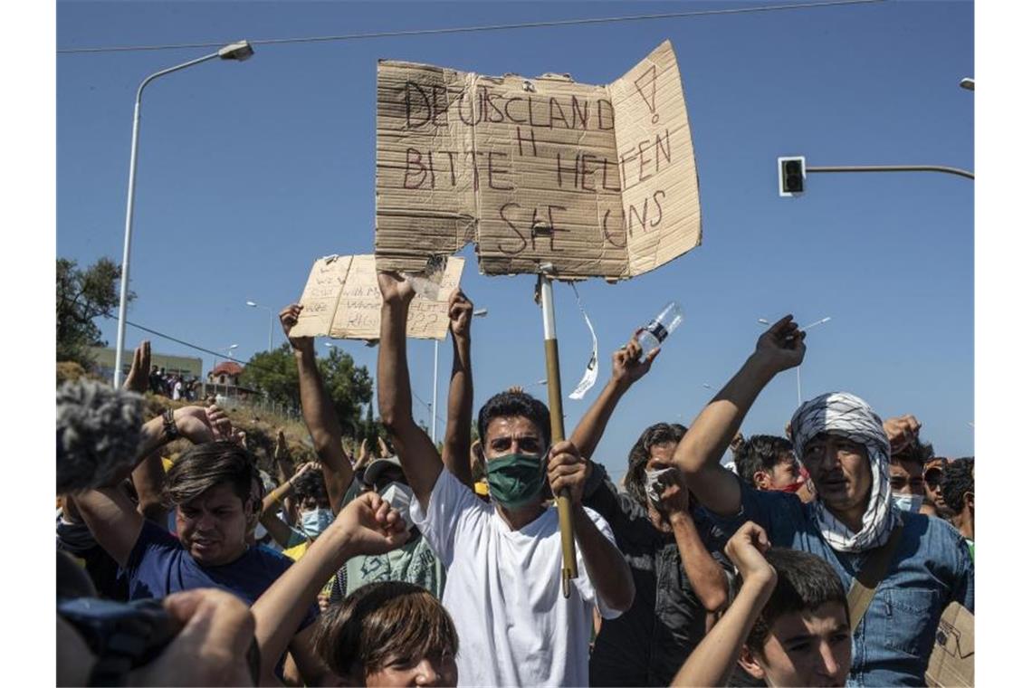 Deutschland nimmt 408 Flüchtlingsfamilien auf Ein Flüchtling auf Lesbos hält ein Plakat mit der Aufschrift „Deutschland, bitte helfen sie uns“. FGriechenland helfen“). Foto: Petros Giannakouris/AP/dpa