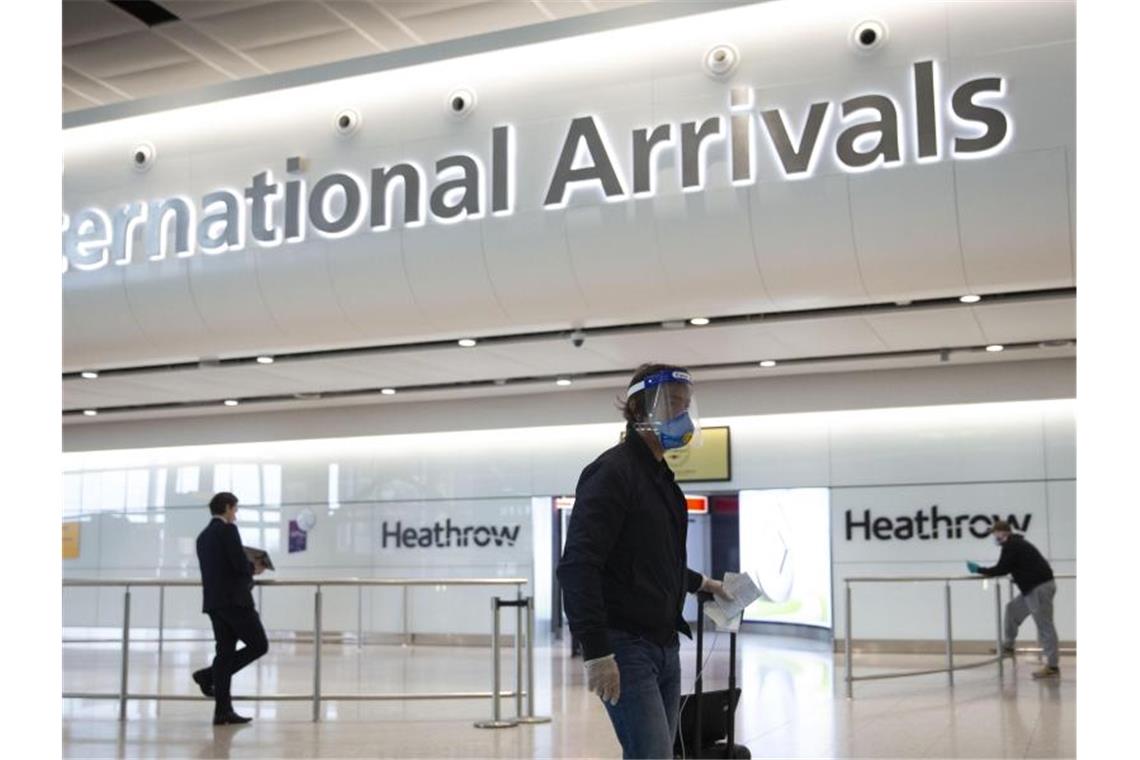 Ein Fluggast mit Mundschutz und Visier geht durch den Flughafen Heathrow. Foto: Matt Dunham/AP/dpa