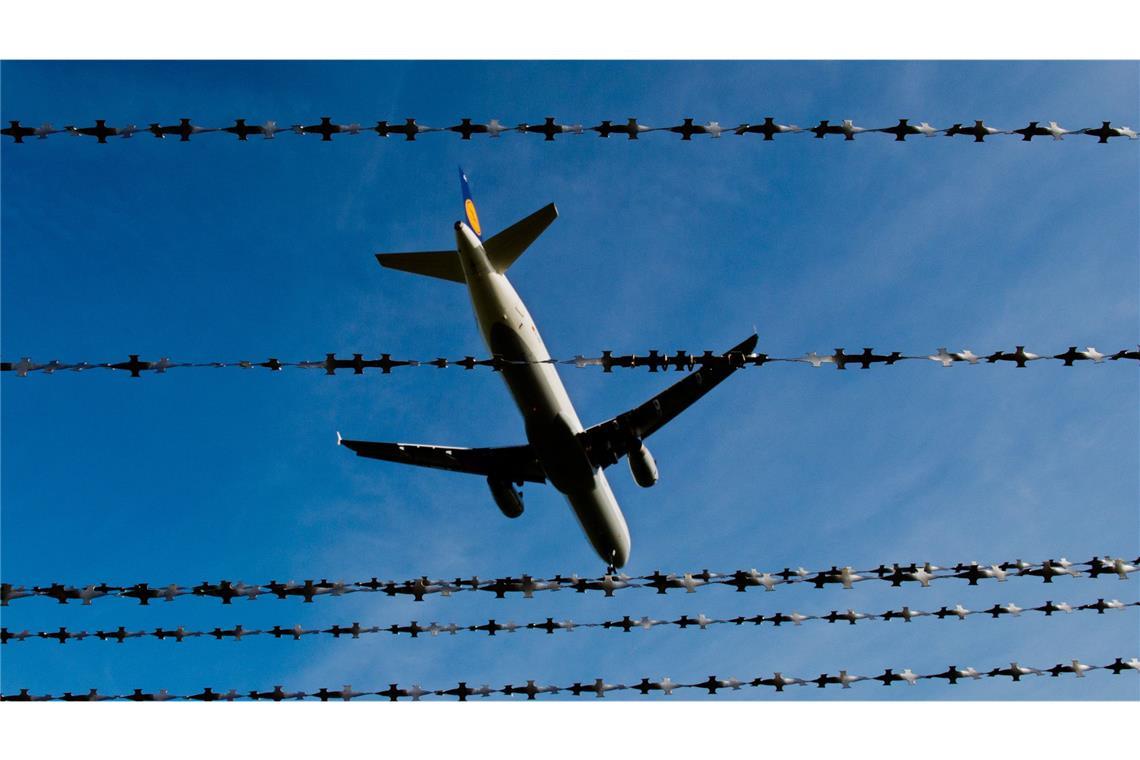 Ein Flugzeug fliegt hinter Stacheldraht. (Symbolfoto)