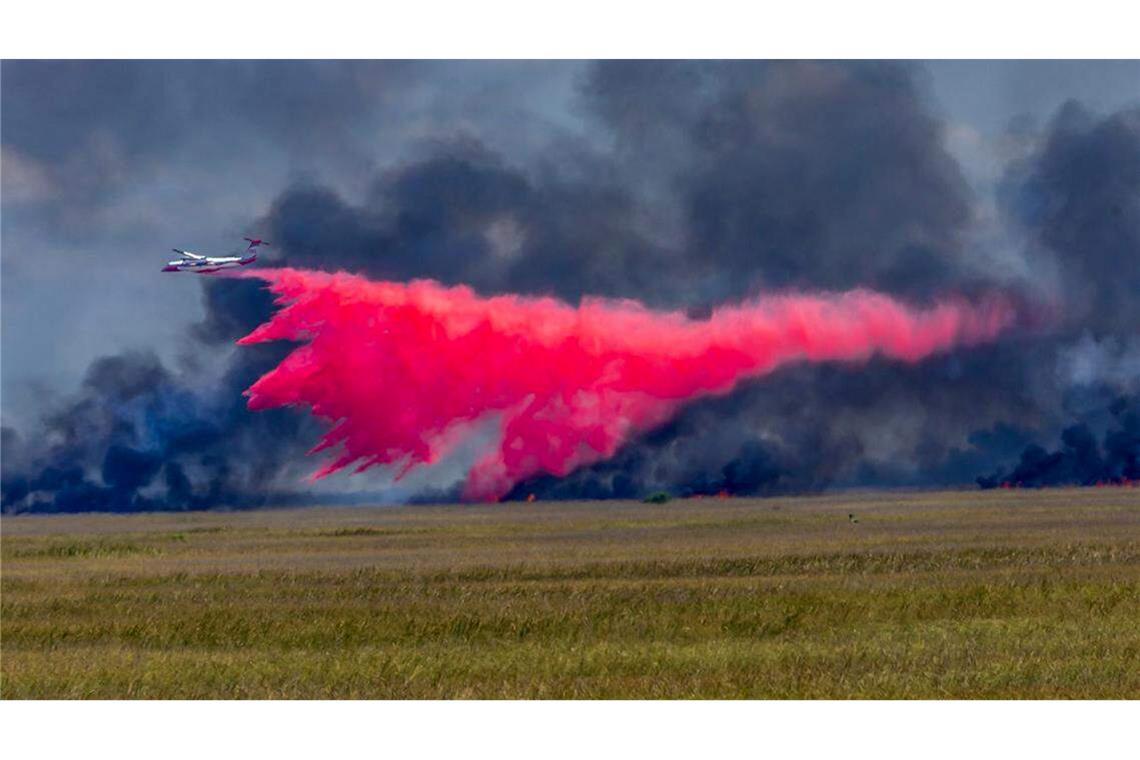 Ein Flugzeug wirft Feuerschutzmittel auf ein großes Waldfeuer.