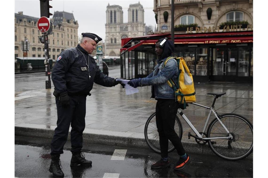 Ein französischer Polizeibeamter überprüft in Paris die Genehmigung eines Passanten, sich weiter als einen Kilometer vom Wohnort zu entfernen. Foto: Francois Mori/AP/dpa