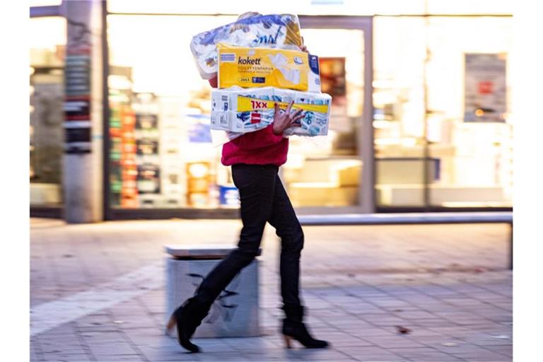Ein Frau läuft mit dem Arm voller Klopapierrollen aus einem Drogeriemarkt heraus. Foto: Axel Heimken/dpa
