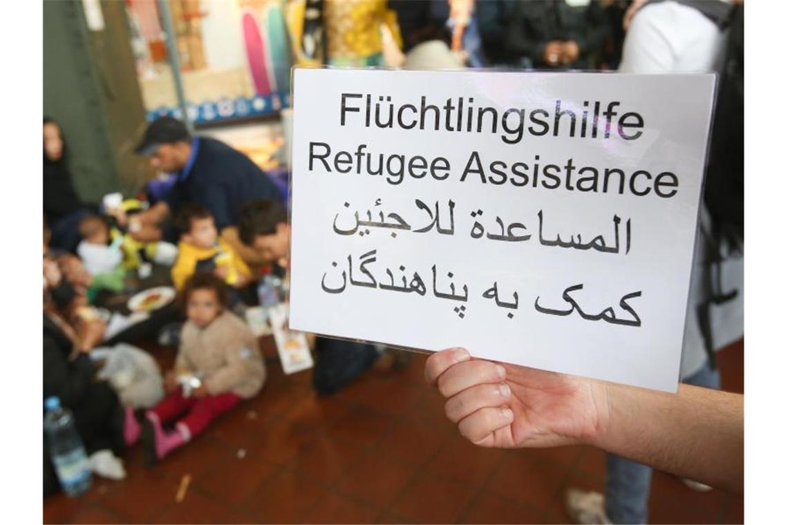 Ein freiwilliger Helfer hält 2015 im Hauptbahnhof in Hamburg ein Schild auf deutsch, englisch und arabisch, auf der Hilfe für Flüchtlinge angeboten wird. Foto: Bodo Marks/dpa