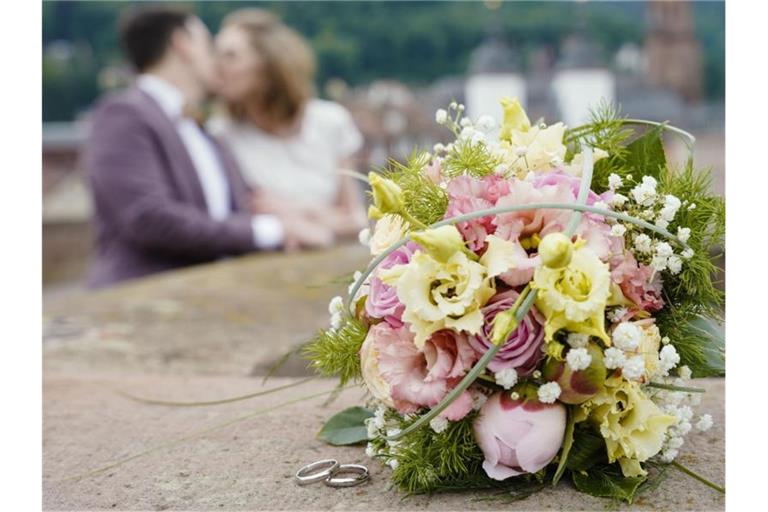 Ein frisch vermähltes Brautpaar küsst sich hinter ihrem Blumenstrauß und den beiden Eheringen. Foto: Uwe Anspach/dpa/Symbolbild