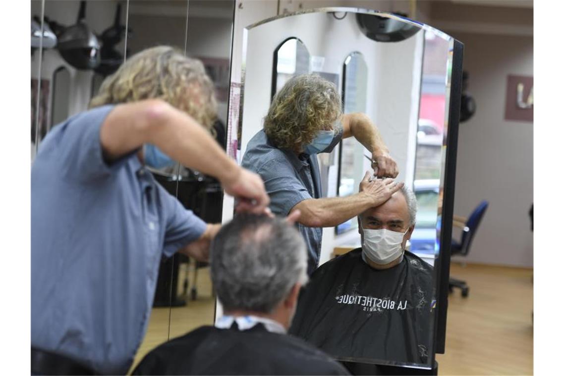 Ein Friseurmeister schneidet in seinem Salon einem Kunden die Haare. Foto: Roberto Pfeil/dpa/archivbild