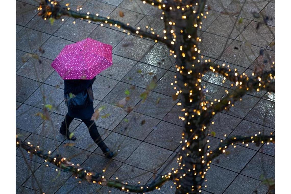 Ein Fußgänger läuft am frühen morgen mit einem Regenschirm durch die beleuchtete Königsstraße. Foto: Tom Weller/dpa