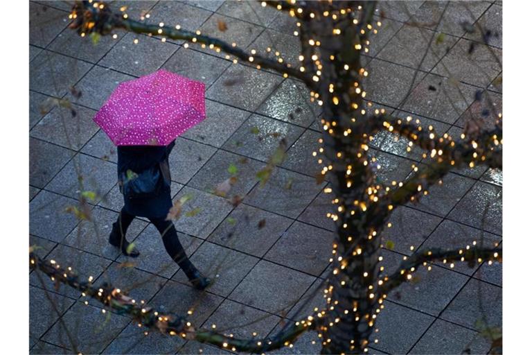 Ein Fußgänger läuft am frühen morgen mit einem Regenschirm durch die beleuchtete Königsstraße. Foto: Tom Weller/dpa