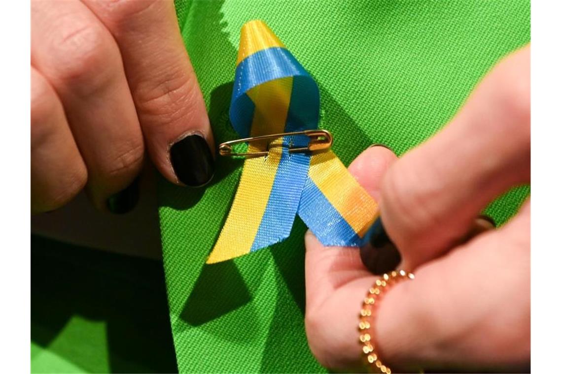 Berliner Modewoche als Zeichen für Freiheit Ein Gast steckt sich aus Solidarität eine Schleife mit der ukrainischen Flagge an. Foto: Jens Kalaene/dpa-Zentralbild/dpa