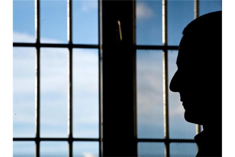 Ein Gefängnisinsasse sitzt in einer JVA vor einem vergitterten Fenster. Foto: Daniel Naupold/dpa/Archivbild