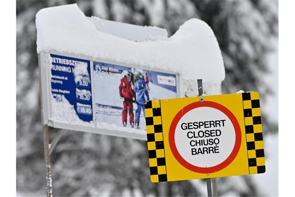 Ein gelbes Hinweisschild mit der Aufschrift „Gesperrt, Closed, Chiuso, Barre“ steht auf der gesperrten Liftanlage im Skigebiet Kranzberg oberhalb von Mittenwald. Foto: Peter Kneffel/dpa