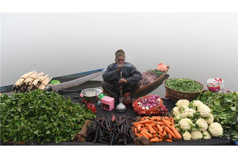Ein Gemüsehändler raucht eine Wasserpfeife, während er an einem nebligen Tag am Ufer eines Sees im indischen Srinagar auf Kunden wartet.
