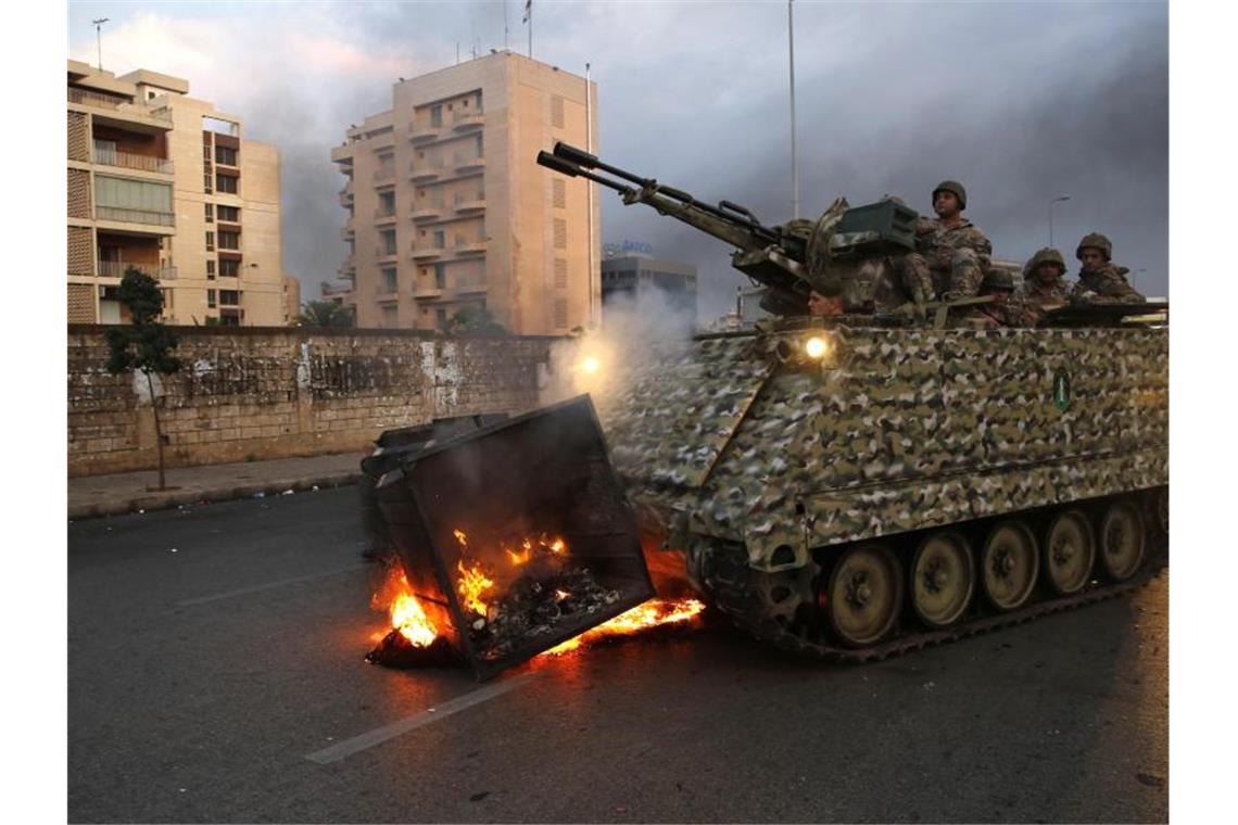 Ein gepanzertes Fahrzeug der Armee beseitigt eine brennende Mülltonne. Seit Tagen kommt es im Libanon zu Massenprotesten gegen die Regierung. Foto: Hussein Malla/AP/dpa