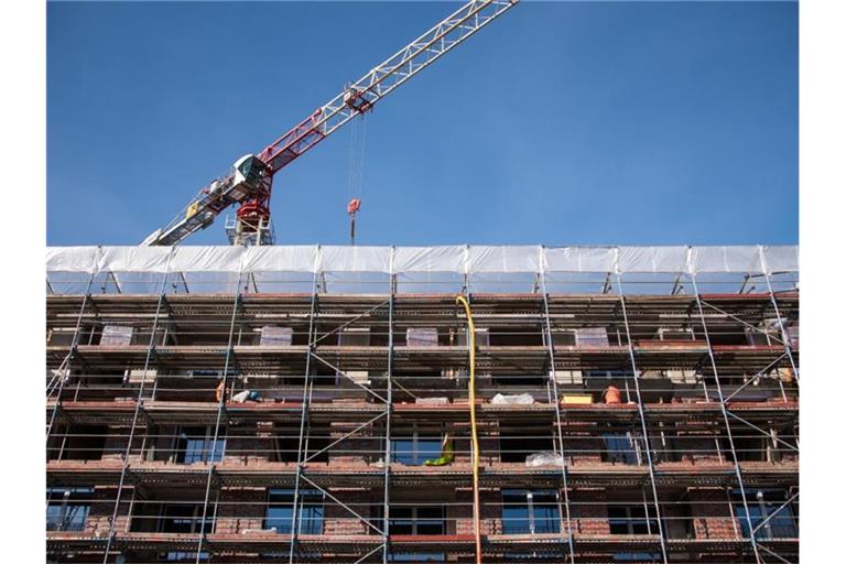 Ein Gerüst ist auf einer Baustelle an einem Neubau von einem Mehrfamilienhaus installiert, über dem Gebäude ist ein Baukran zu sehen. Foto: Daniel Bockwoldt/dpa