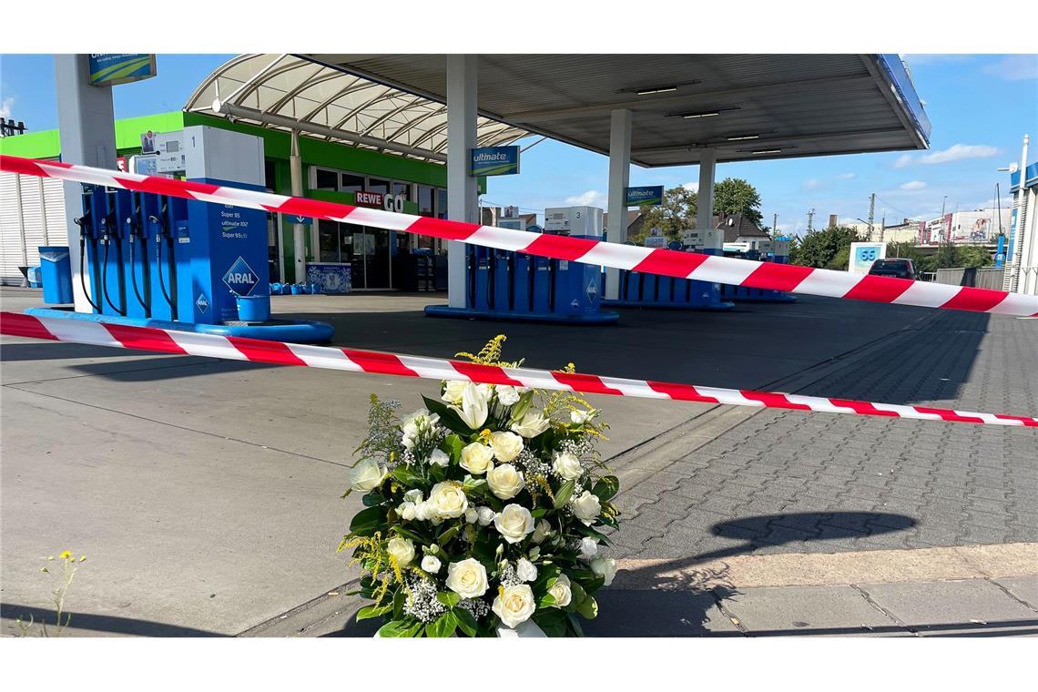 Ein großer Blumenkranz steht vor der überfallenen Tankstelle.