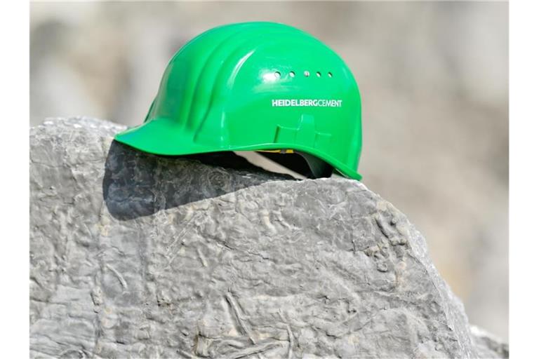 Ein grüner Arbeitshelm mit der Aufschrift „HeidelbergCement“ liegt im Steinbruch. Foto: Uwe Anspach/dpa