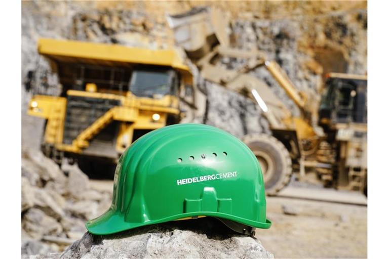 Ein grüner Schutzhelm mit der Aufschrift „HeidelbergCement“ liegt im Steinbruch des Baustoffkonzerns. Foto: Uwe Anspach/dpa/Archivbild