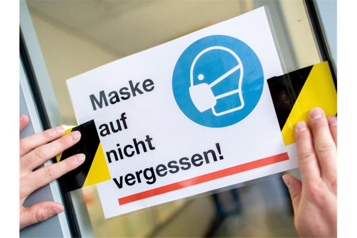 Ein Hausmeister bringt in der Schule ein Hinweisschild zum Tragen einer Maske an. Foto: Hauke-Christian Dittrich/dpa/Symbolbild