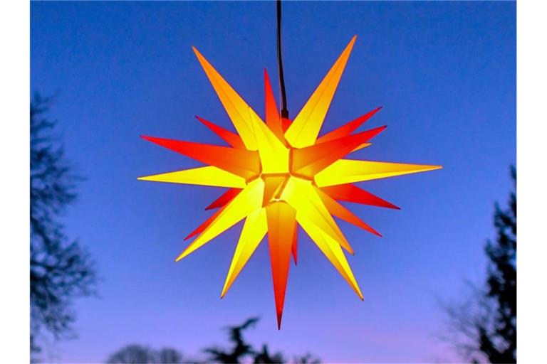 Ein Herrnhuter Stern leuchtet zur blauen Stunde. Foto: Patrick Pleul/zb/dpa/Archivbild