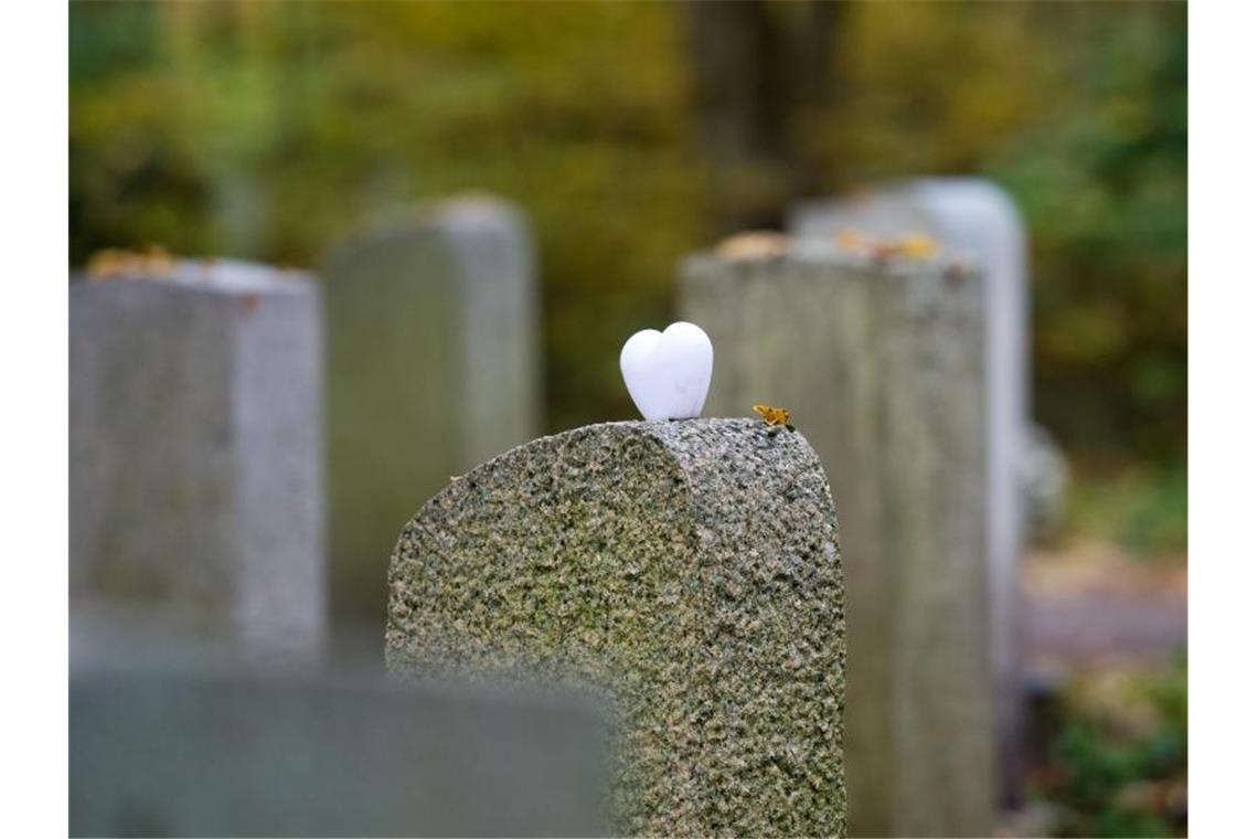 Ein herzförmiger Stein liegt einem Grabstein auf einem Friedhof. Foto: Inga Kjer/dpa