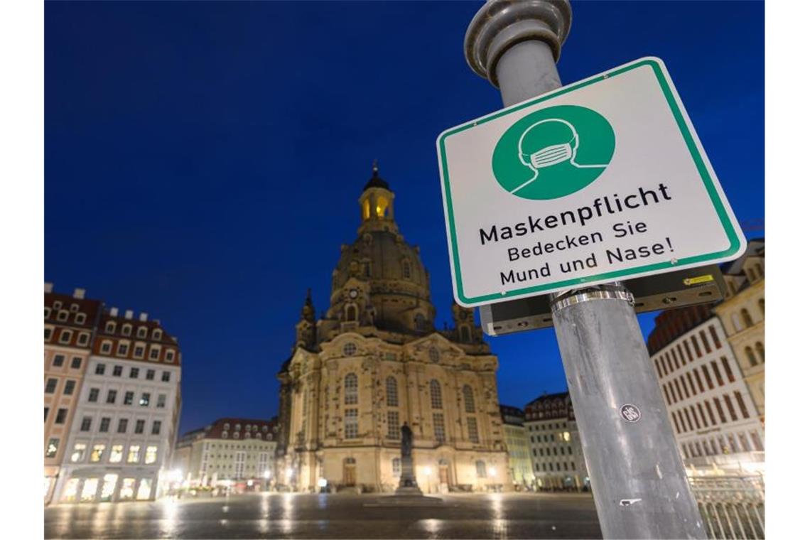 Ein Hinweisschild auf die Maskenpflicht hängt auf dem Neumarkt vor der Frauenkirche an einem Lampenmast. Foto: Robert Michael/dpa-Zentralbild/dpa