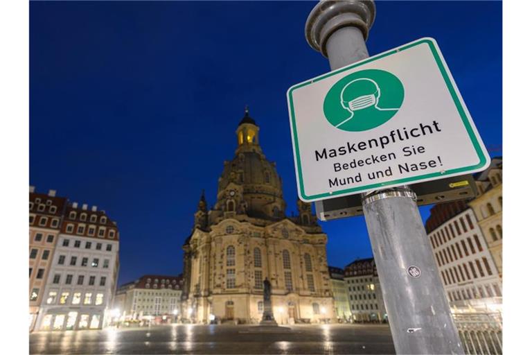 Ein Hinweisschild auf die Maskenpflicht hängt auf dem Neumarkt vor der Frauenkirche an einem Lampenmast. Foto: Robert Michael/dpa-Zentralbild/dpa