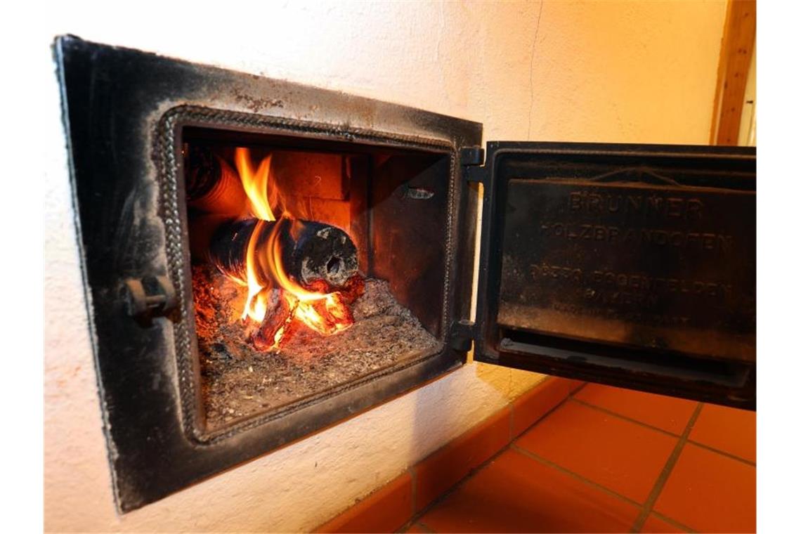 Ein Holzofen wird vom Hausflur aus mit Holzbriketts geheizt. Foto: Karl-Josef Hildenbrand/dpa