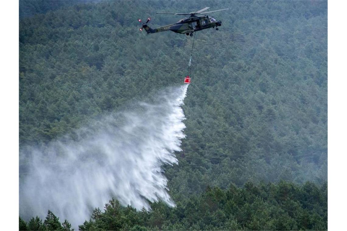 Ein Hubschrauber der Bundeswehr vom Typ NH90 mit einem Löschwasser-Behälter wirft über einer Brandstelle Löschwasser ab. Foto: Jens Büttner