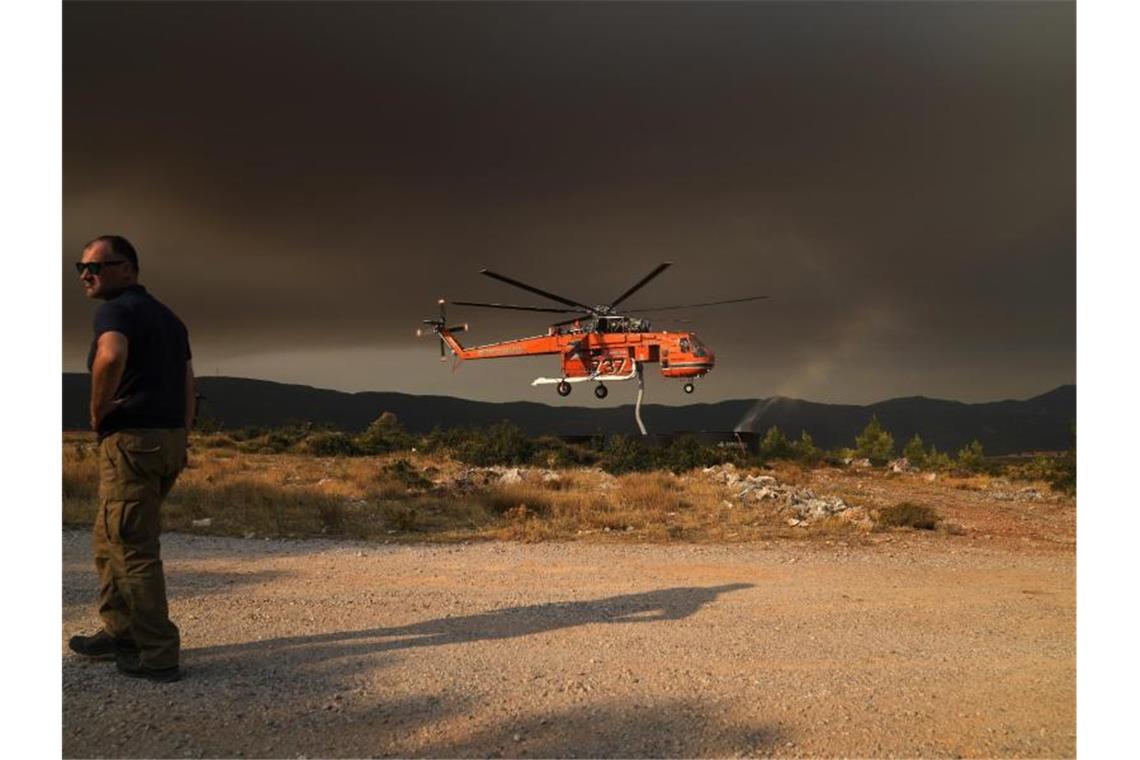 Ein Hubschrauber füllt einen Wassertank, um Vilia vor den Flammen zu schützen. Foto: Thanassis Stavrakis/AP/dpa