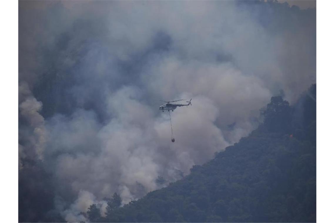 Ein Hubschrauber transportiert im türkischen Turgut Löschwasser zu einem Waldbrand. Foto: Emre Tazegul/AP/dpa