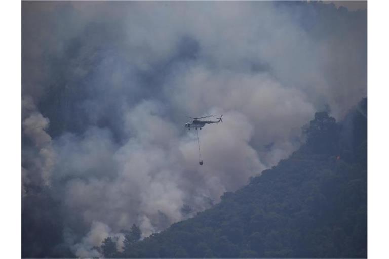 Ein Hubschrauber transportiert im türkischen Turgut Löschwasser zu einem Waldbrand. Foto: Emre Tazegul/AP/dpa
