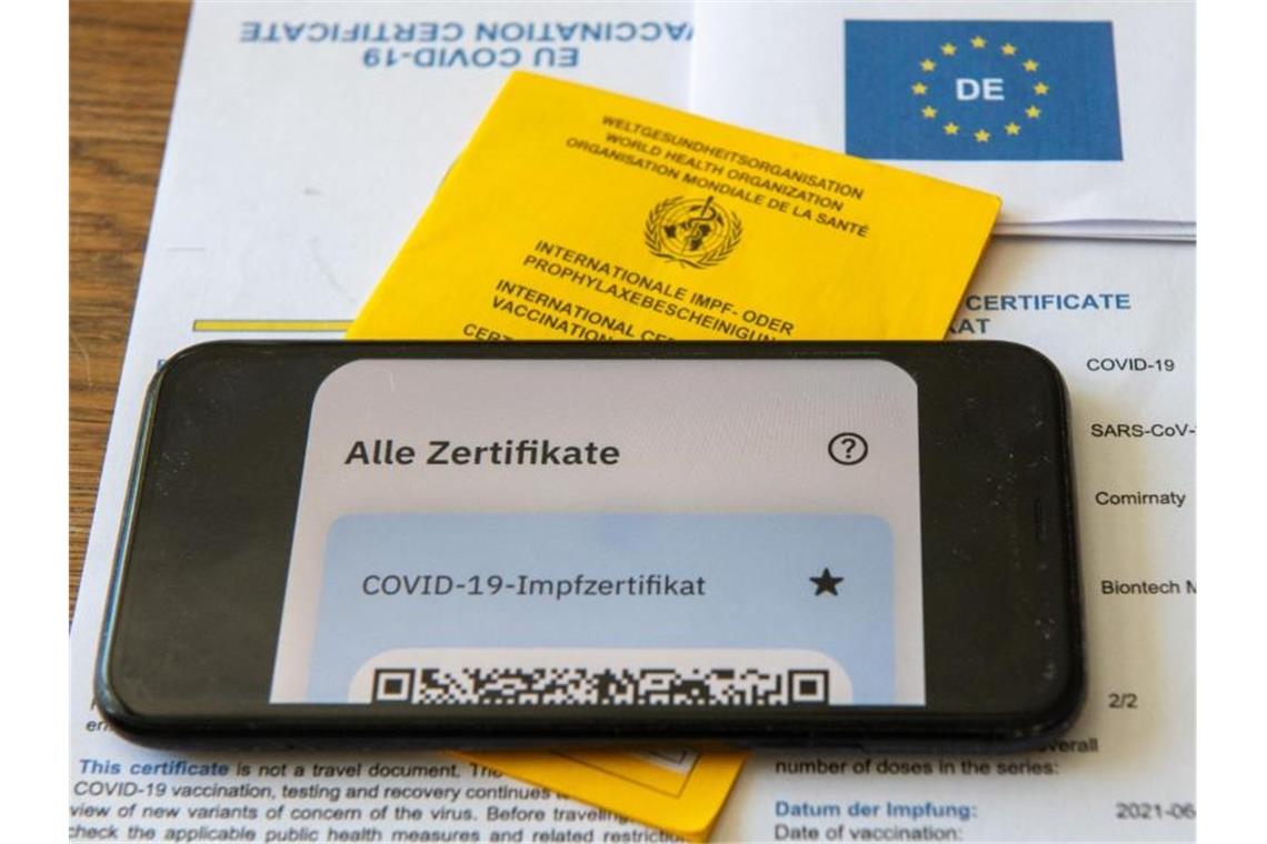 Ein Impfpass und ein Smartphone, auf dem die App CovPass läuft, liegen auf einem Impfzertifikat, das von einer Apotheke ausgestellt wurde. Foto: Stefan Puchner/dpa