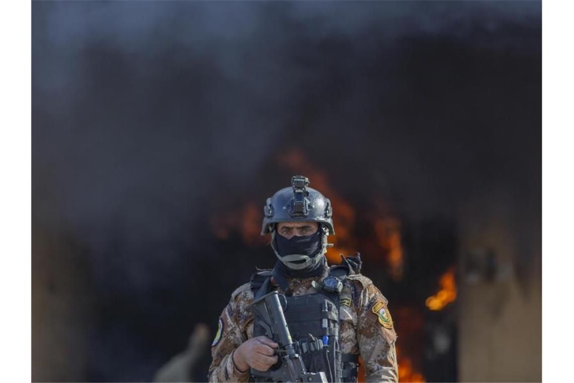 Ein irakischer Soldat am Neujahrstag vor der Rauchwolke eines nahe der US-Botschaft in Bagdad brennenden Feuers. Foto: Nasser Nasser/AP/dpa