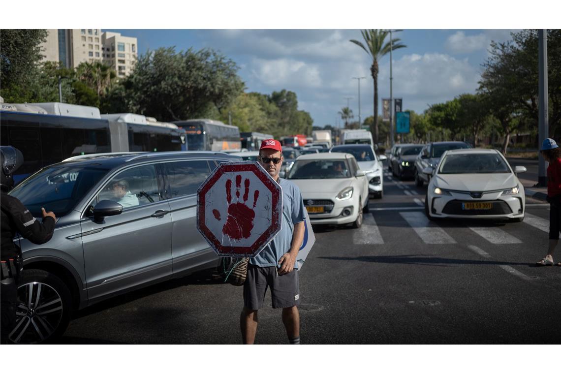 Streik in Israel aus Solidarität mit den Hamas-Geiseln Ein israelischer Demonstrant geht mit einem Schild auf einer Straße, während Autos sich stauen.