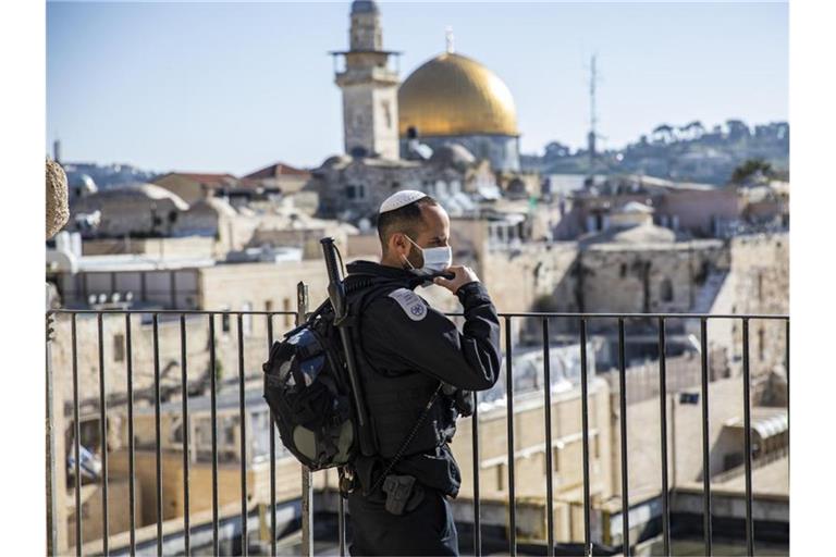 Ein israelischer Polizist mit Mundschutz steht in der Altstadt Wache. Im Hintergrund der Felsendom auf dem Tempelberg. Foto: Ilia Yefimovich/dpa