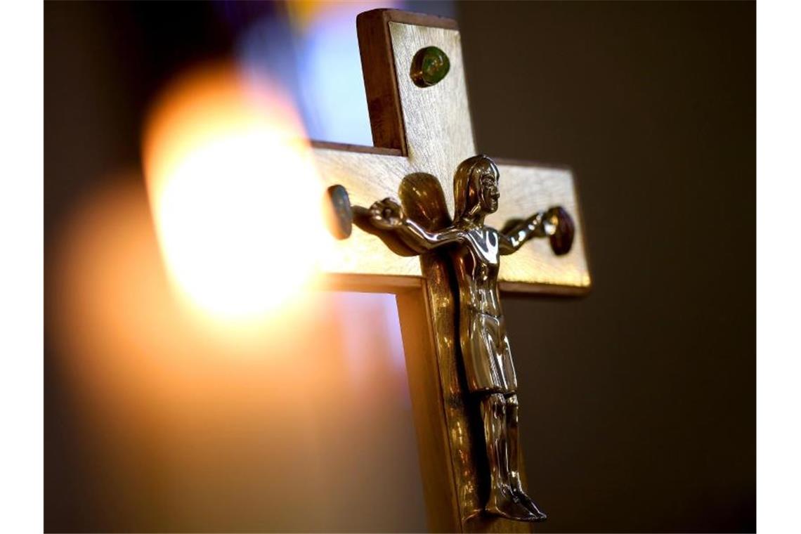 Ein Jesuskreuz und eine brennende Kerze stehen in einer Kirche. Foto: Ronny Hartmann/dpa/Archivbild