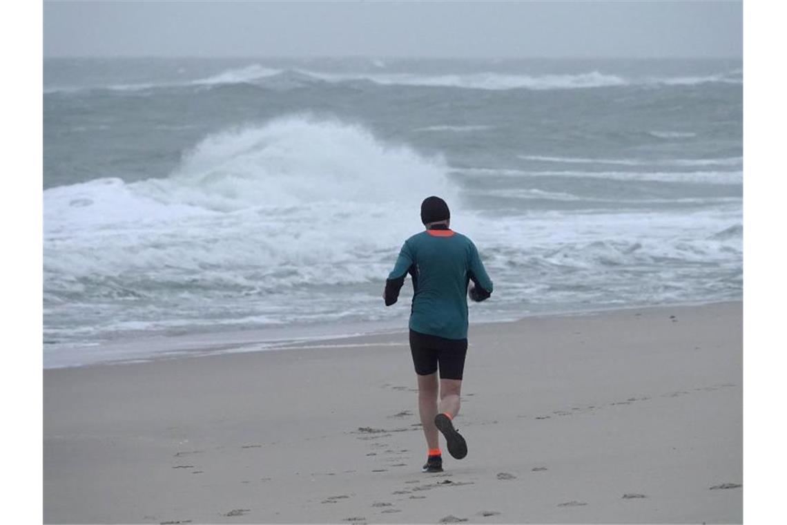 Ein Jogger ist bei stürmischem Wetter am Strand von Westerland auf Sylt unterwegs. Foto: Bodo Marks/dpa