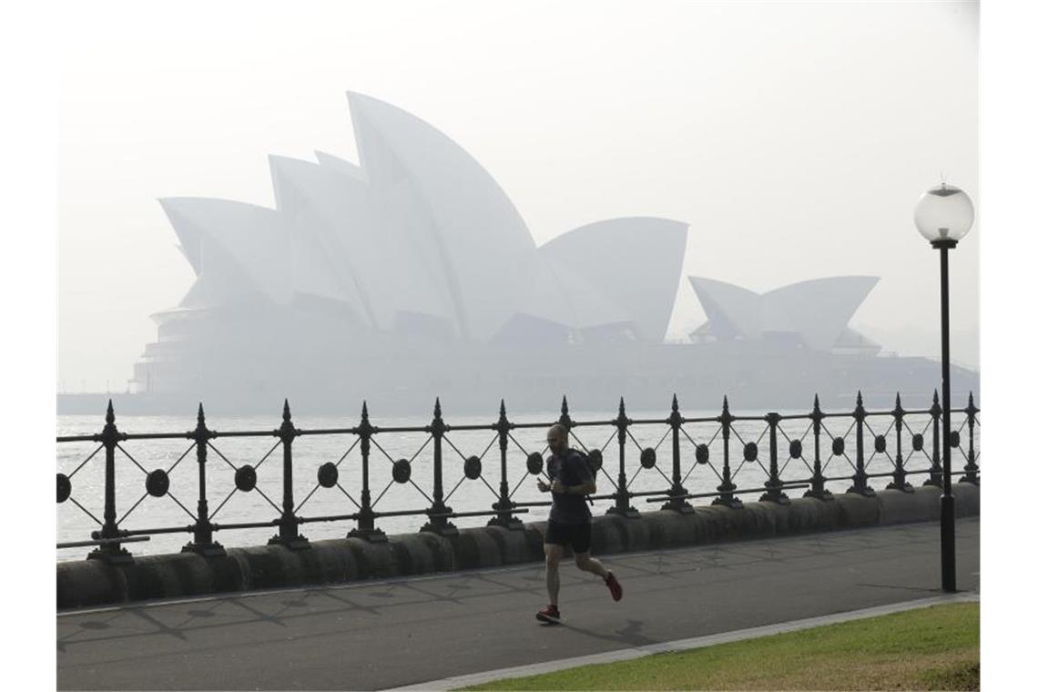Ein Jogger läuft am Morgen, während Rauchschleier über der Sydney Opera House hängt. Foto: Rick Rycroft/AP/dpa