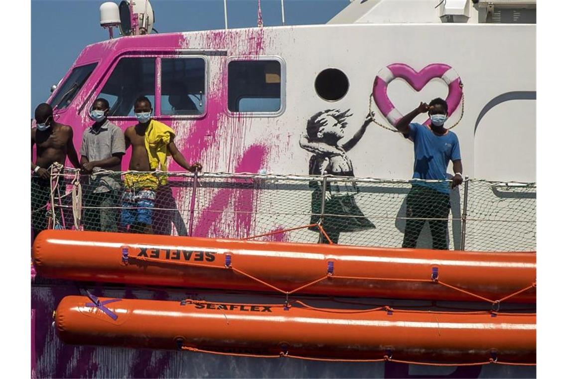 Ein Junge an Bord der „Louise Michel“ winkt der Besatzung des Rettungsschiffes „Astral“ zu. Das Rettungsschiff „Louise Michel“ kann sich nach Angaben der Besatzung mit mehr als 200 Migranten an Bord nicht länger sicher fortbewegen. Foto: Santi Palacios/AP/dpa