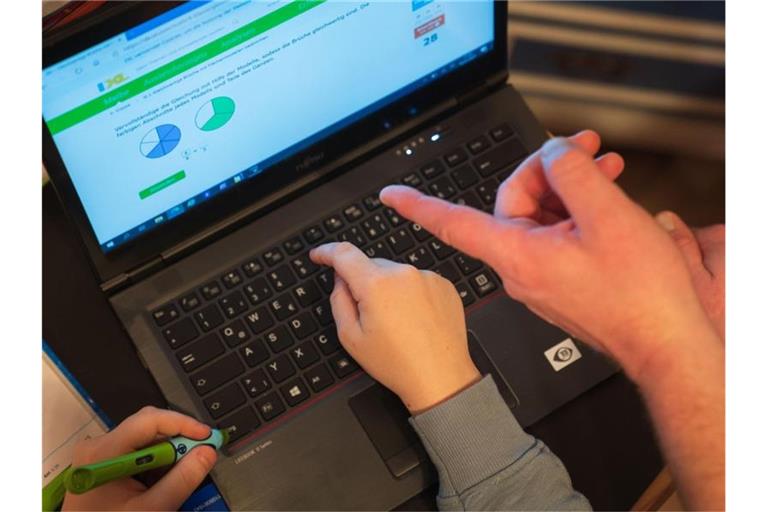 Ein Junge nutzt zusammen mit seinem Vater einen Laptop für den Heimunterricht. Foto: Nicolas Armer/dpa